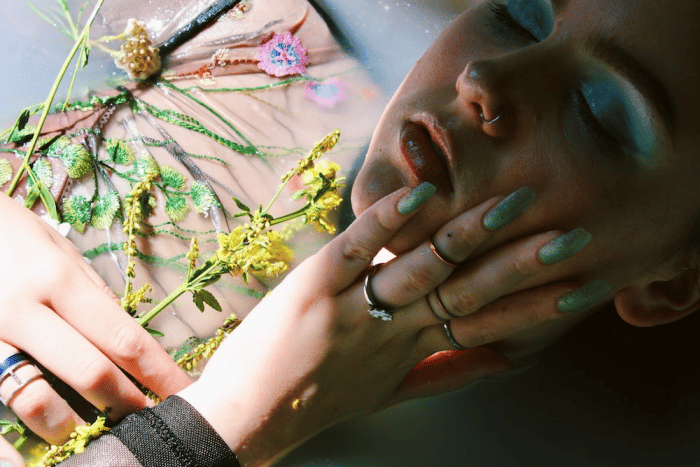 A Woman Touching her Face with a Hand Featuring Custom Press On Nails in a Cyan Colour