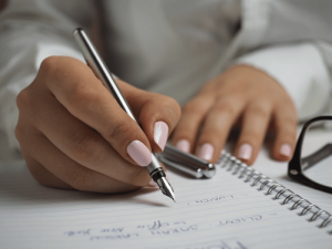 a woman writing in a notebook with healthy, strong nails