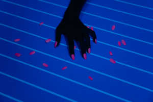 A Darkened Hand with Pink Manicured Press-on Nails Surrounded by the Same Scattered Nails Against a Blue-lined Backdrop